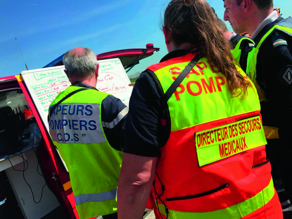 Photographie de sapeurs-pompiers en gilets de coordination devant un tableau blanc, sur le lieu d'une intervention